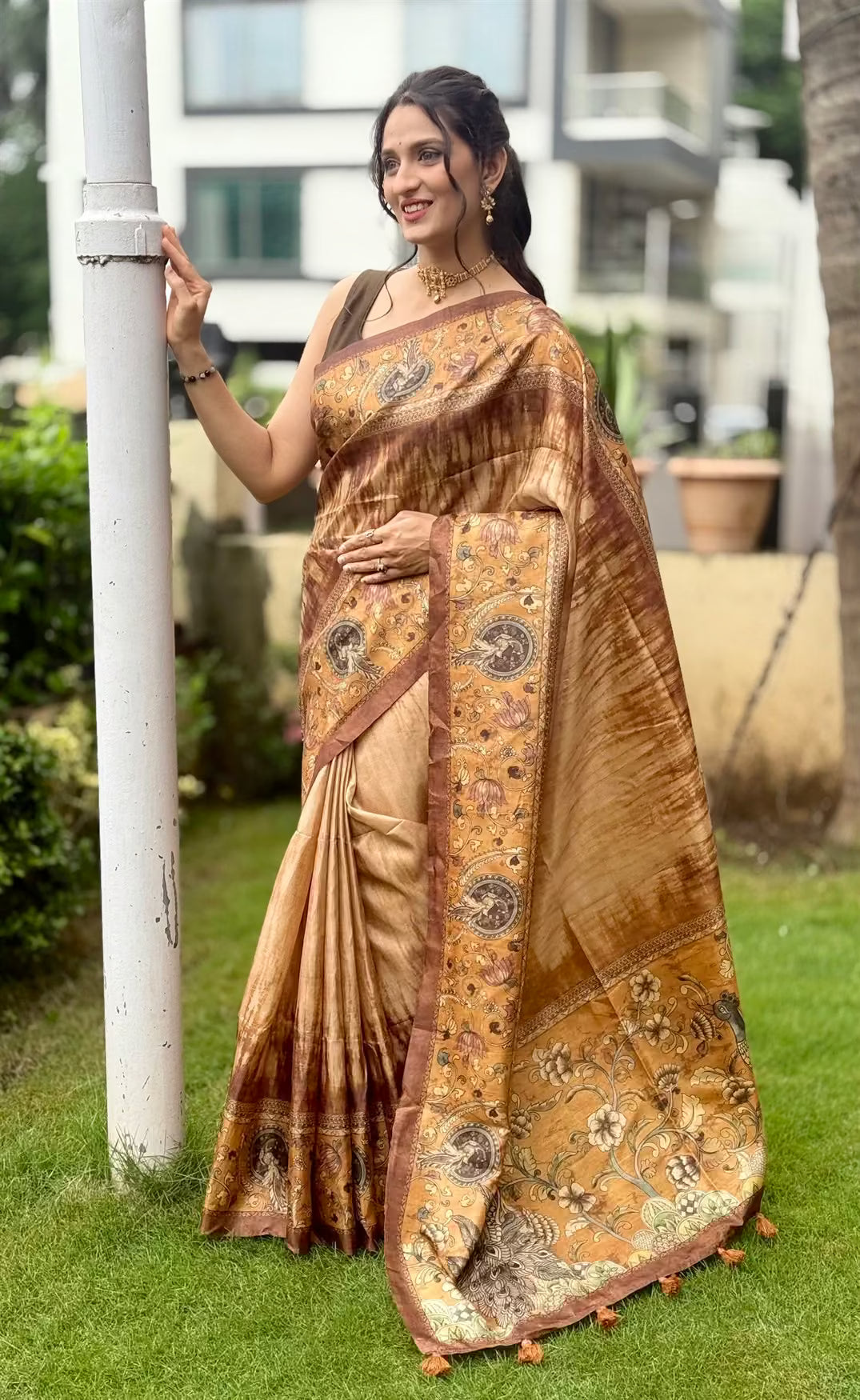 Woman wearing peacock pallu printed saree in gold and deep brown tones.