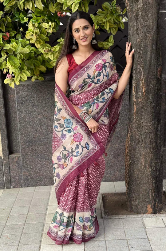 Woman in a floral border saree standing next to a tree