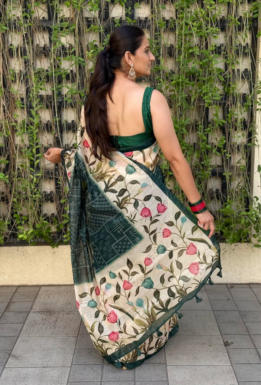 Woman wearing a floral saree with a green border against a textured wall.