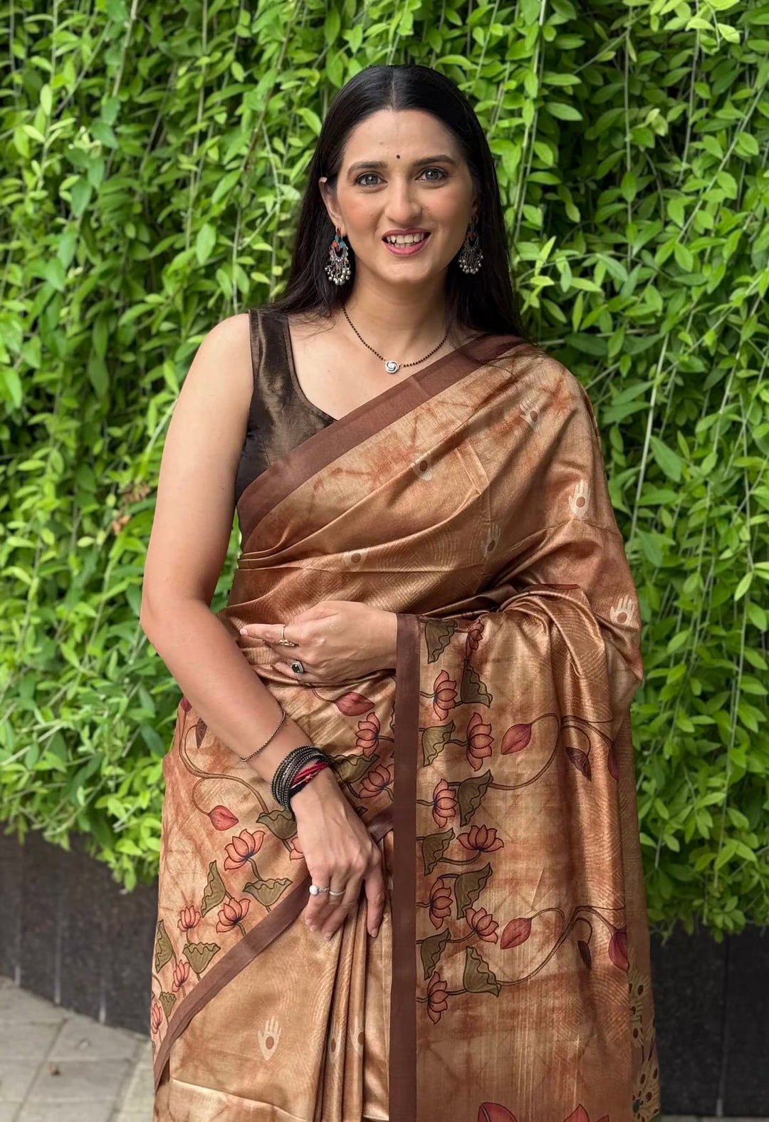 A women wearing copper color saree in kalamkari lotus print with brown border.
